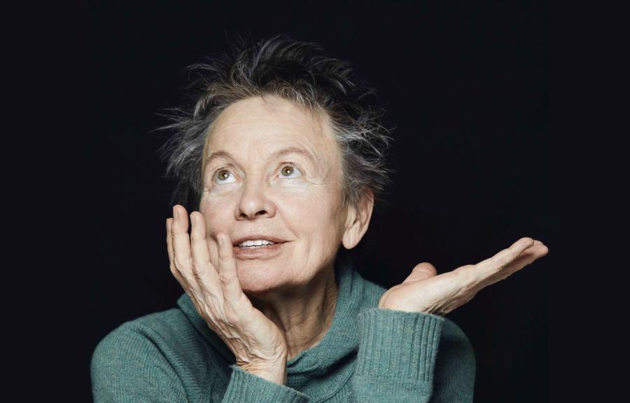 Portrait of Laurie Anderson looking skyward with a smile and expressive hand gesture